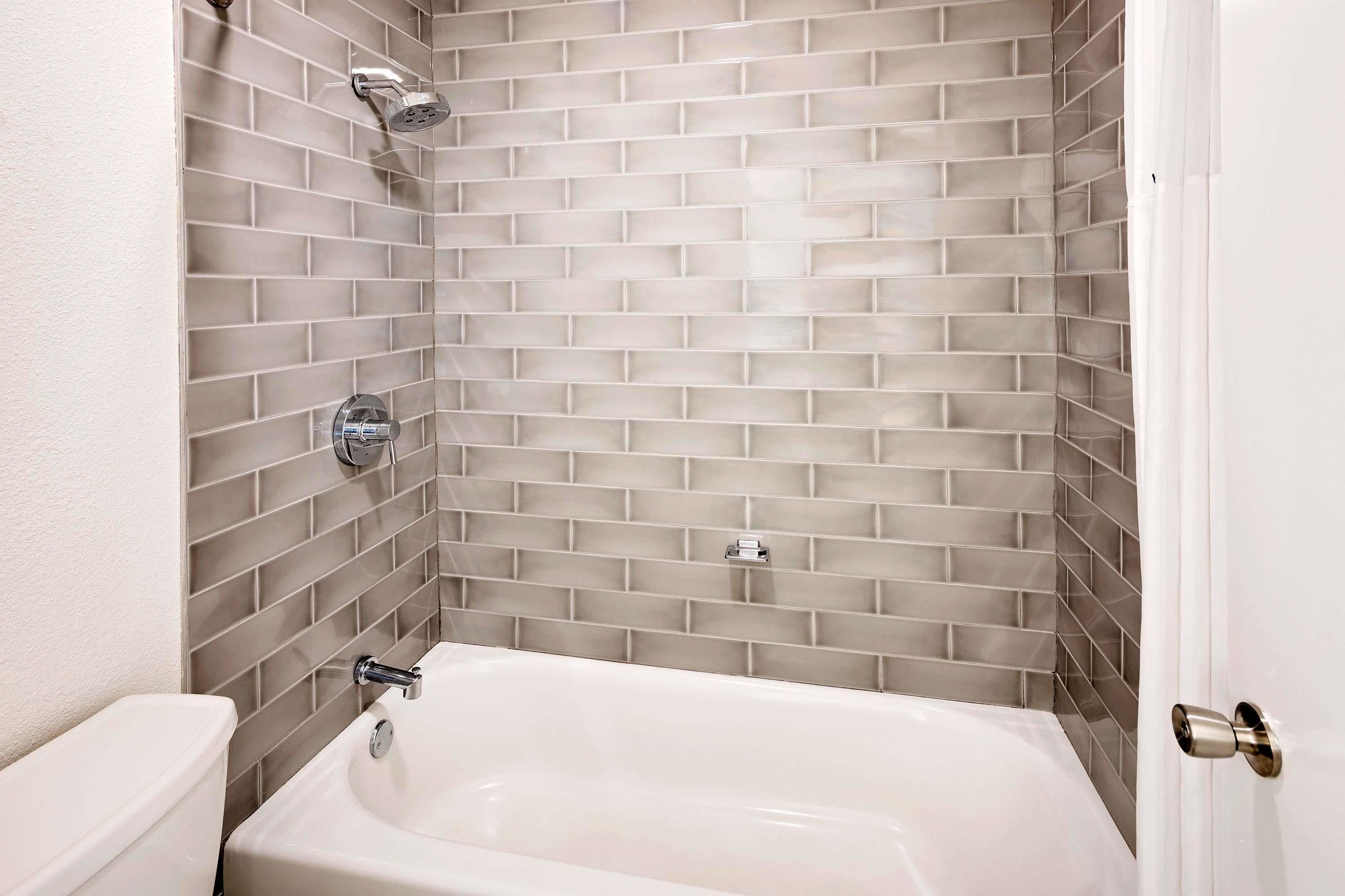 Un baño con una bañera blanca, un inodoro y una ducha con grifo cromado.