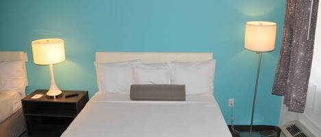 A hotel room with a bed, two bedside tables, a lamp on each table, a patterned throw blanket, and a window with curtains.