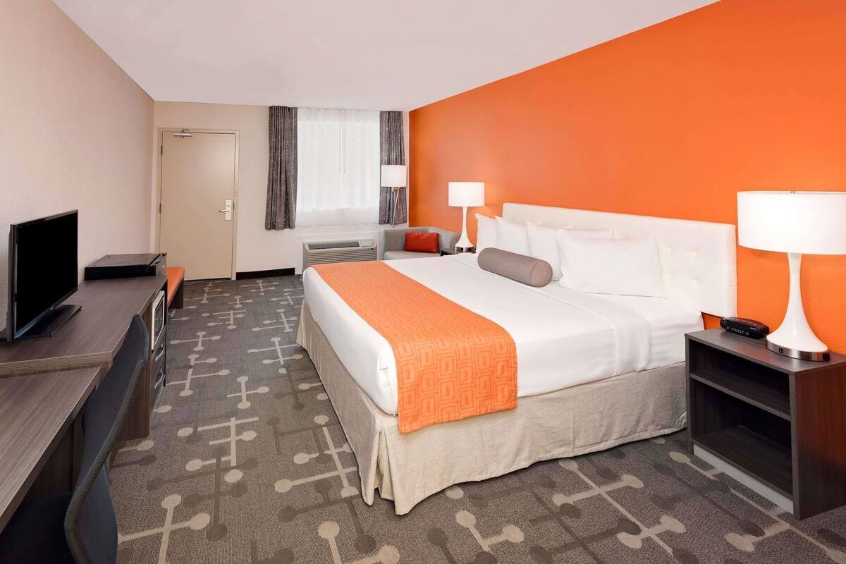A hotel room with a bed, bedside tables, a desk, a television, and a window with curtains.