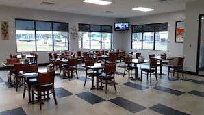 A spacious dining area with multiple tables and chairs, large windows offering a view of the parking lot, and a television mounted on the wall. - Howard Johnson by Wyndham Florence (Florence)