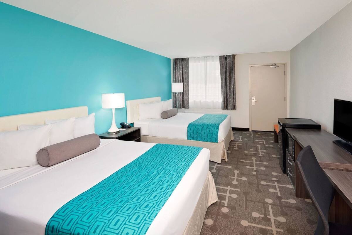 A hotel room with two beds, a desk with a TV, a door, and a window with curtains.