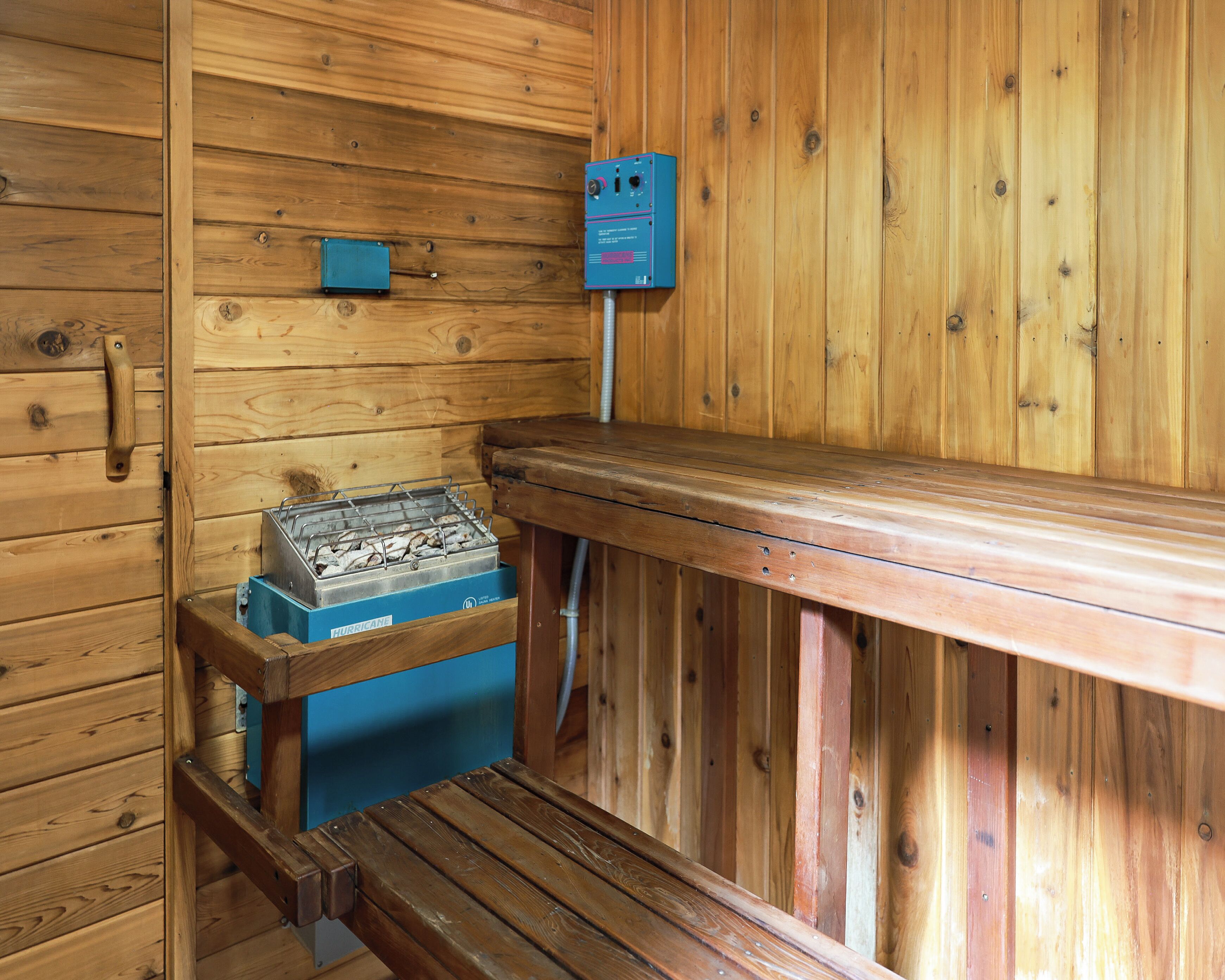 A wooden sauna with a bench, a heater, and a control panel.