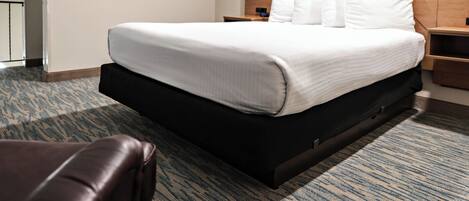 A hotel room with a large bed, a flat-screen TV mounted on the wall, a wooden headboard, and a patterned carpet.