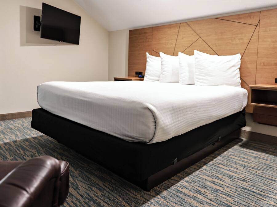 A hotel room with a large bed, a flat-screen TV mounted on the wall, a wooden headboard, and a patterned carpet.