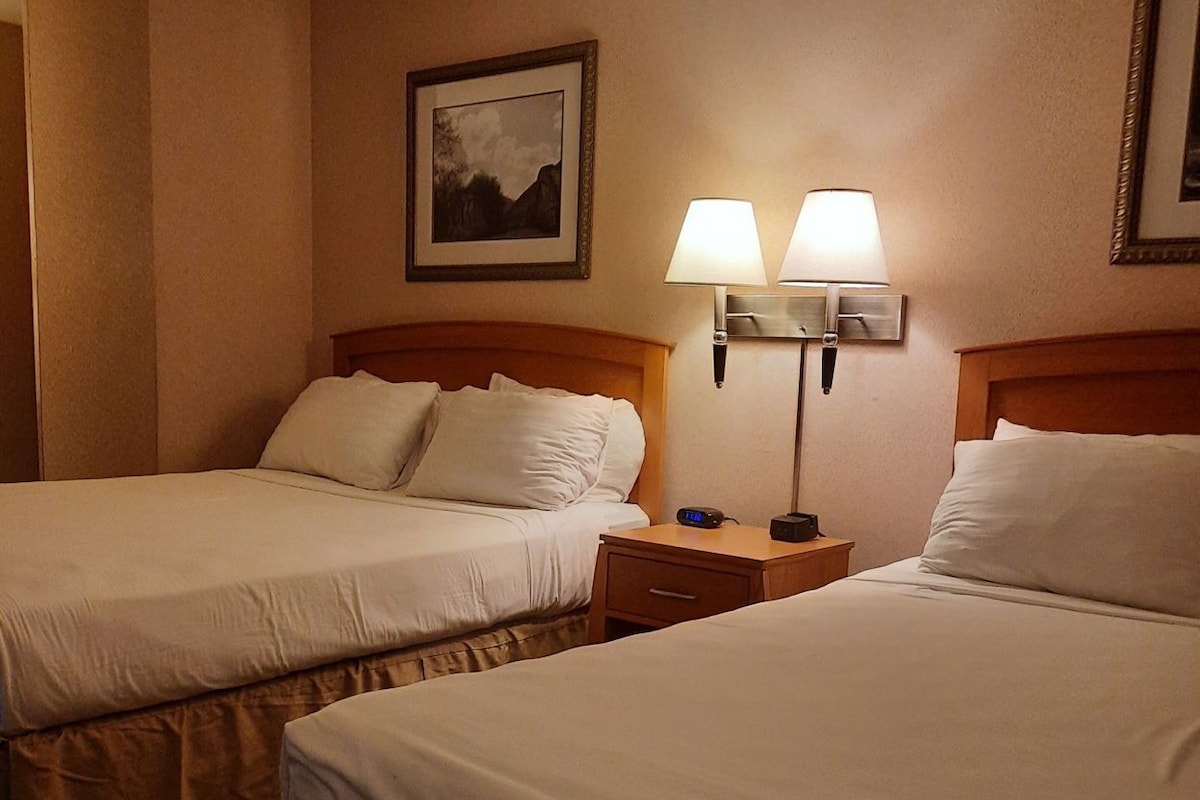 A hotel room with two beds, a nightstand with a lamp, and a framed picture on the wall.
