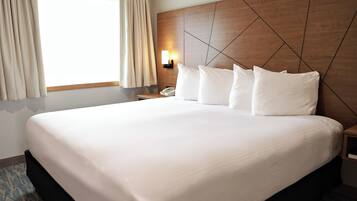 Una habitación de hotel con una cama grande, un cabecero de madera, una mesita de noche con una lámpara y una ventana con cortinas.