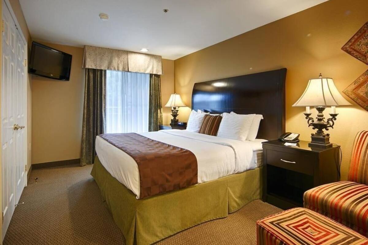 A hotel room with a bed, bedside lamps, a television, a desk with a phone, and a chair.