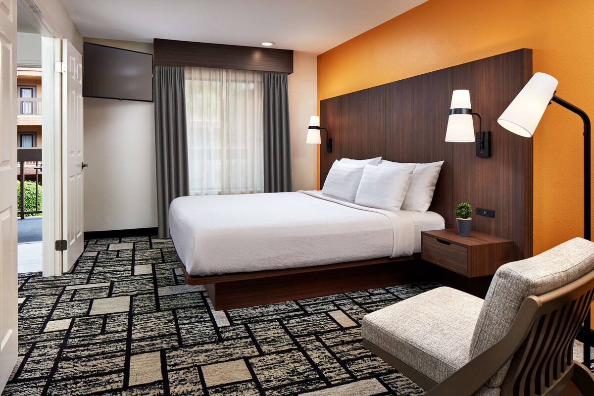 A hotel room with a bed, a chair, a nightstand, a TV, and a window with curtains.