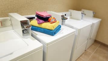 Une rangée de lave-linge à chargement frontal blancs est alignée dans une buanderie dont le sol est carrelé.