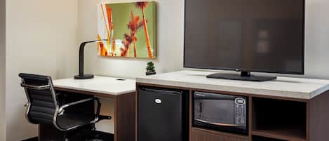 Habitación de hotel con cama, escritorio, monitor de computadora, refrigerador y microondas.
