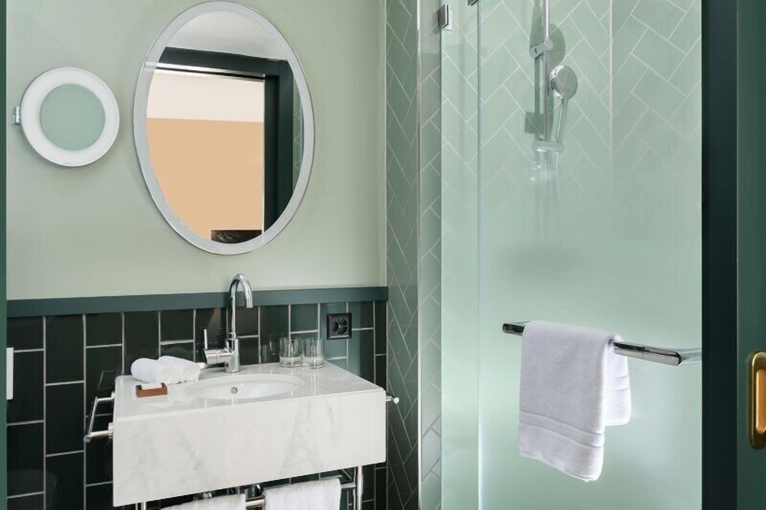 Une salle de bain avec un miroir rond, un lavabo et une douche en verre.