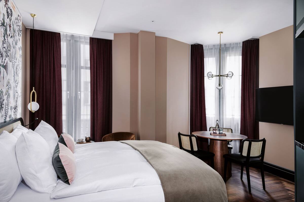 Une chambre d’hôtel avec un grand lit, une table à manger avec des chaises, un lustre et un téléviseur.
