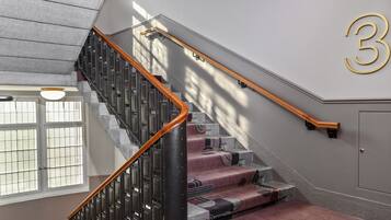 A staircase with a wooden handrail, a number '3' on the wall, and a window with a view of the outside.