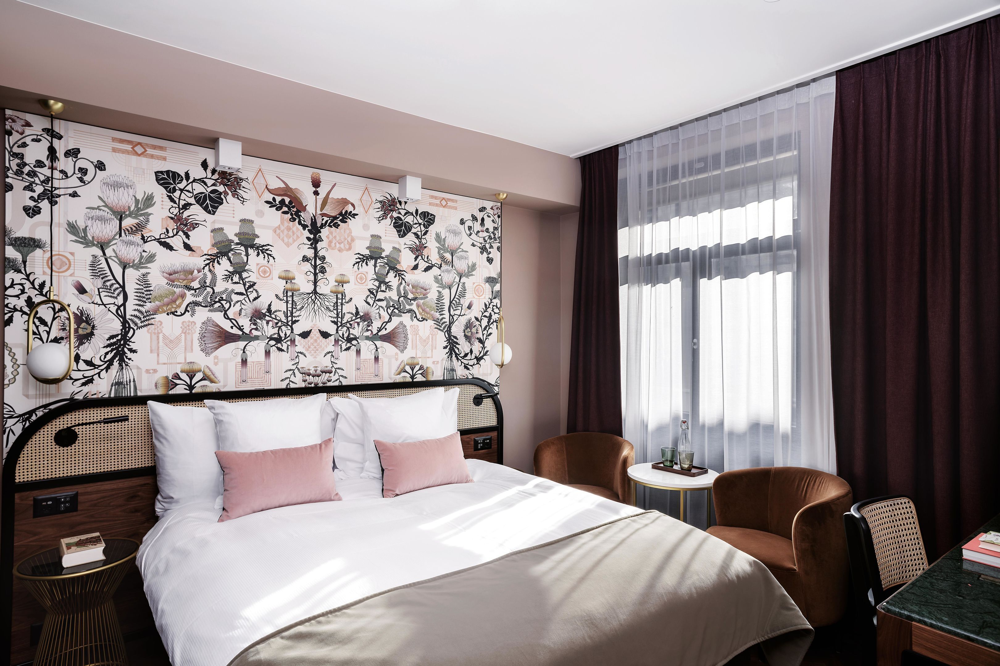 A hotel room with a bed, a chair, a small table, and a window with curtains.