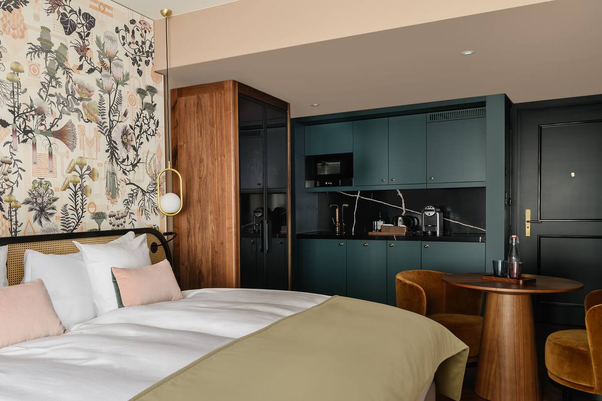 Une chambre d’hôtel comprenant un lit, une armoire en bois, une kitchenette et une table ronde en bois avec des chaises.
