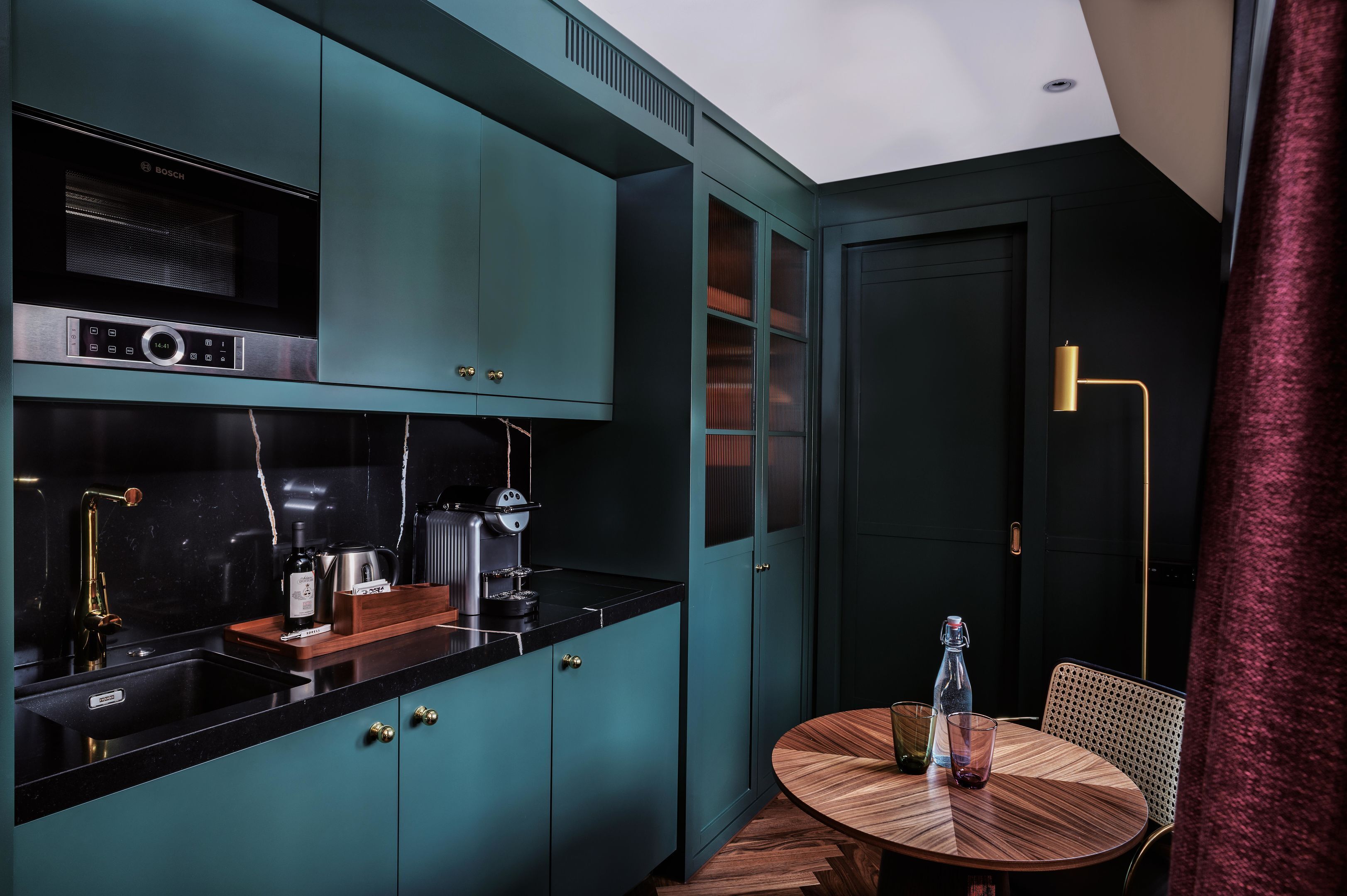 Una cocina moderna con un microondas Bosch, una cafetera y una mesa de madera con una botella y un vaso.