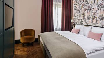 A hotel room with a bed, a chair, a wooden floor, and a floral wallpaper.