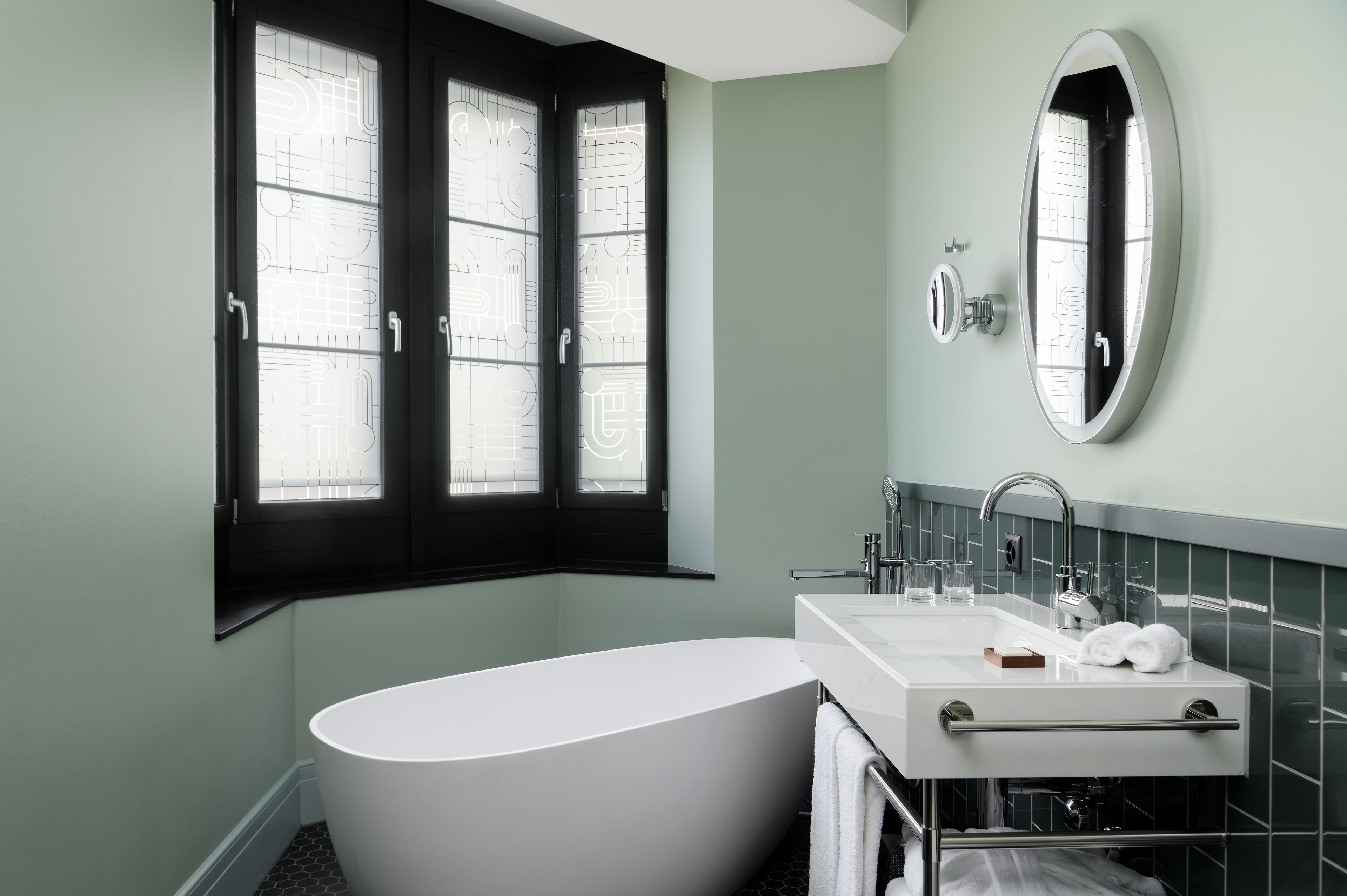 Une salle de bain moderne avec une baignoire sur pieds, un lavabo blanc avec un miroir et une fenêtre dotée de volets noirs.