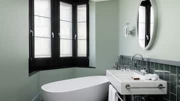 Une salle de bain moderne avec une baignoire sur pieds, un lavabo blanc avec un miroir et une fenêtre dotée de volets noirs.