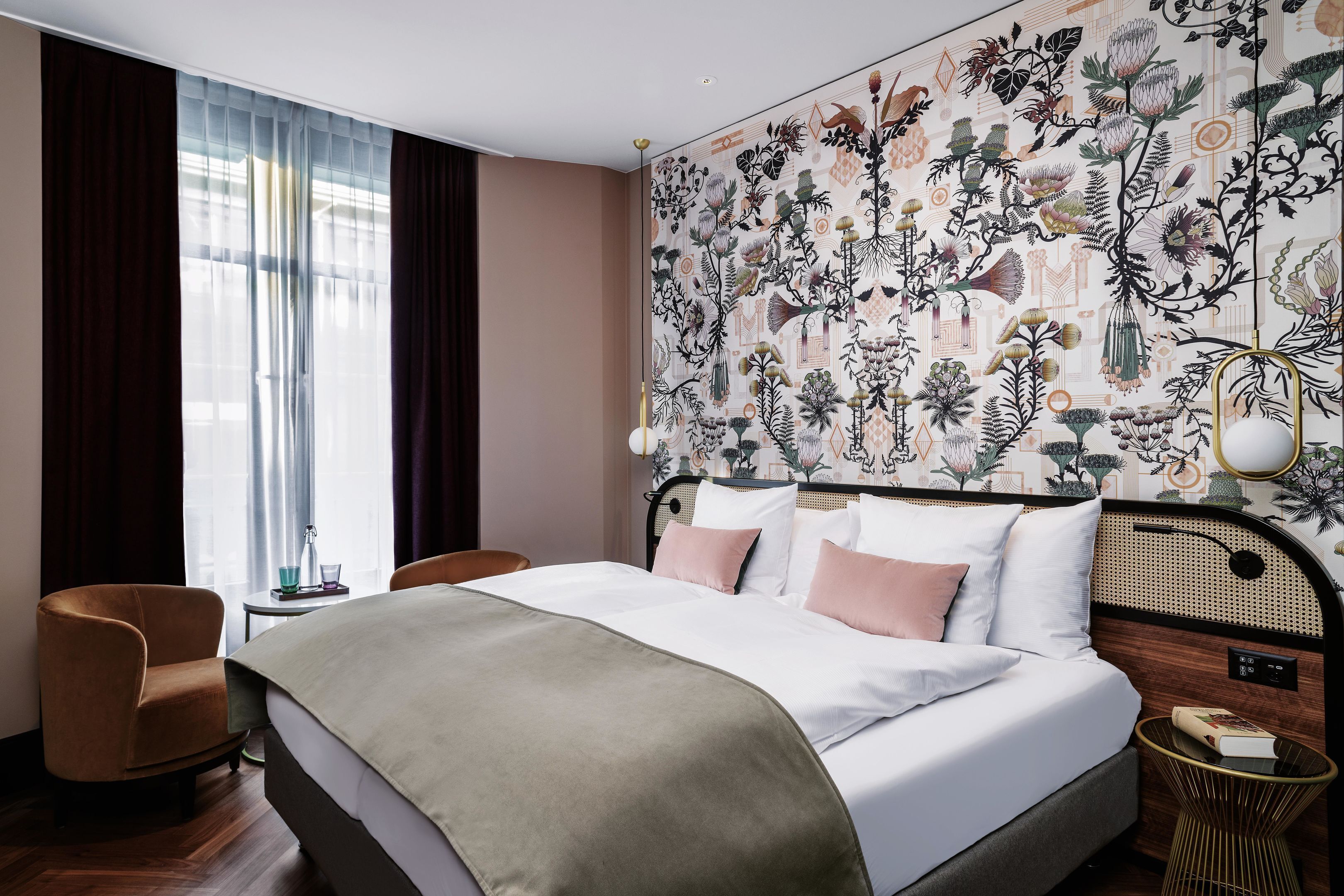 Une chambre d’hôtel avec un grand lit, une chaise, une table de chevet et un mur orné d’un motif floral.