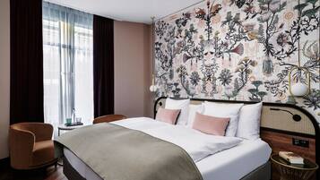 Habitación de hotel con una cama grande, una silla, una mesita de noche y una pared con estampado floral.