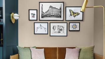 Ein modernes Wohnzimmer mit einem braunen Sofa, zwei Sesseln, einem Couchtisch und einer Stehlampe. An der Wand befinden sich gerahmte Kunstwerke.