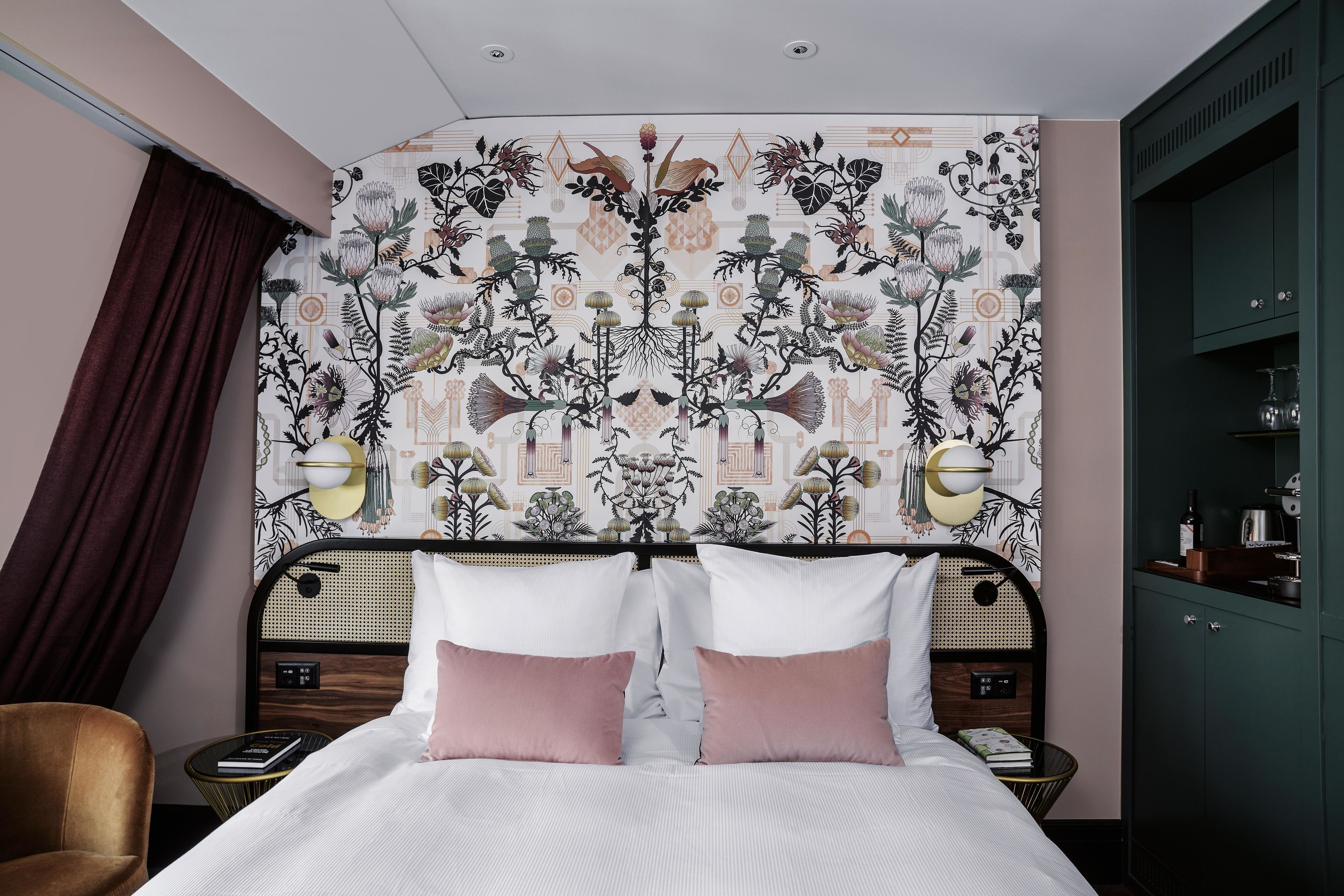 A bedroom with a patterned wallpaper, a bed with two pillows, bedside tables with lamps, and a wardrobe.