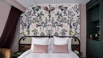 A bedroom with a patterned wallpaper, a bed with two pillows, bedside tables with lamps, and a wardrobe.