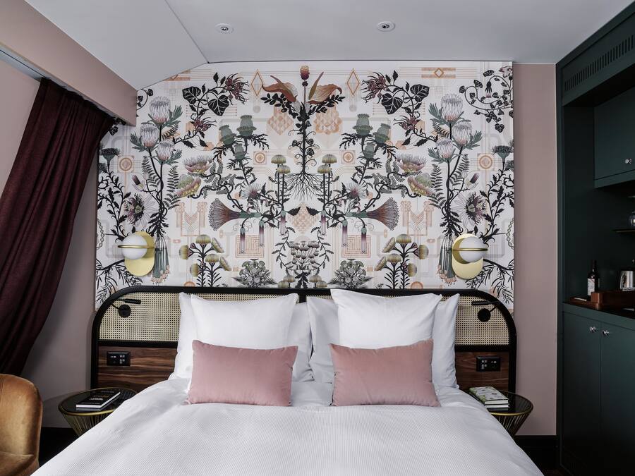 Ein Schlafzimmer mit gemustertem Wandpapier, einem Bett mit zwei Kissen, Nachttischen mit Lampen und einem Kleiderschrank.
