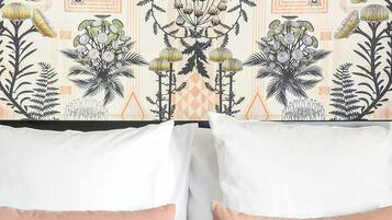A neatly made bed with a patterned headboard, a book, a glass of water, and a tray with a cup and bowl.