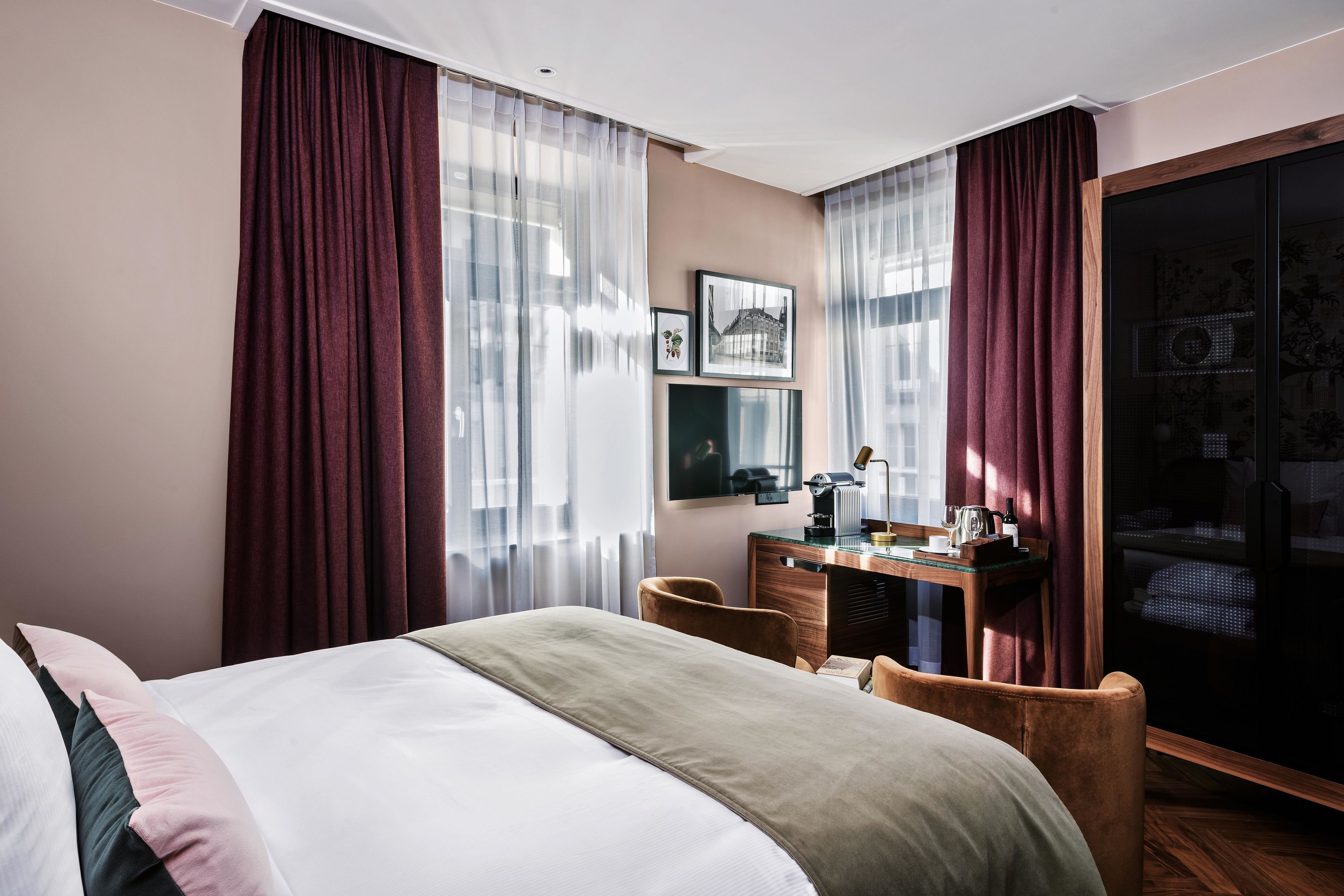 Habitación de hotel con cama, escritorio, silla y un ventanal con cortinas.