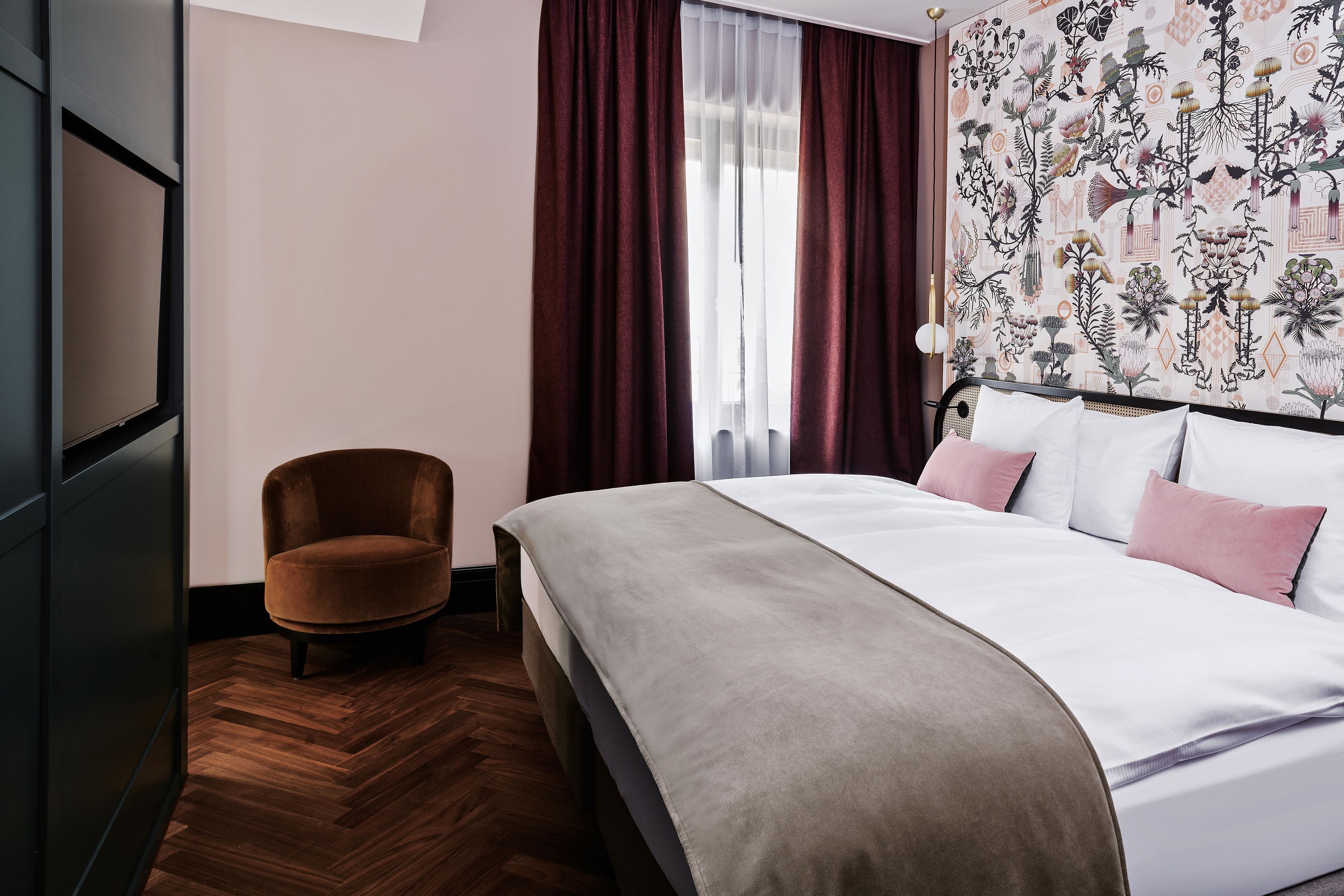 A bedroom with a bed, a chair, a window with curtains, and a patterned wall.