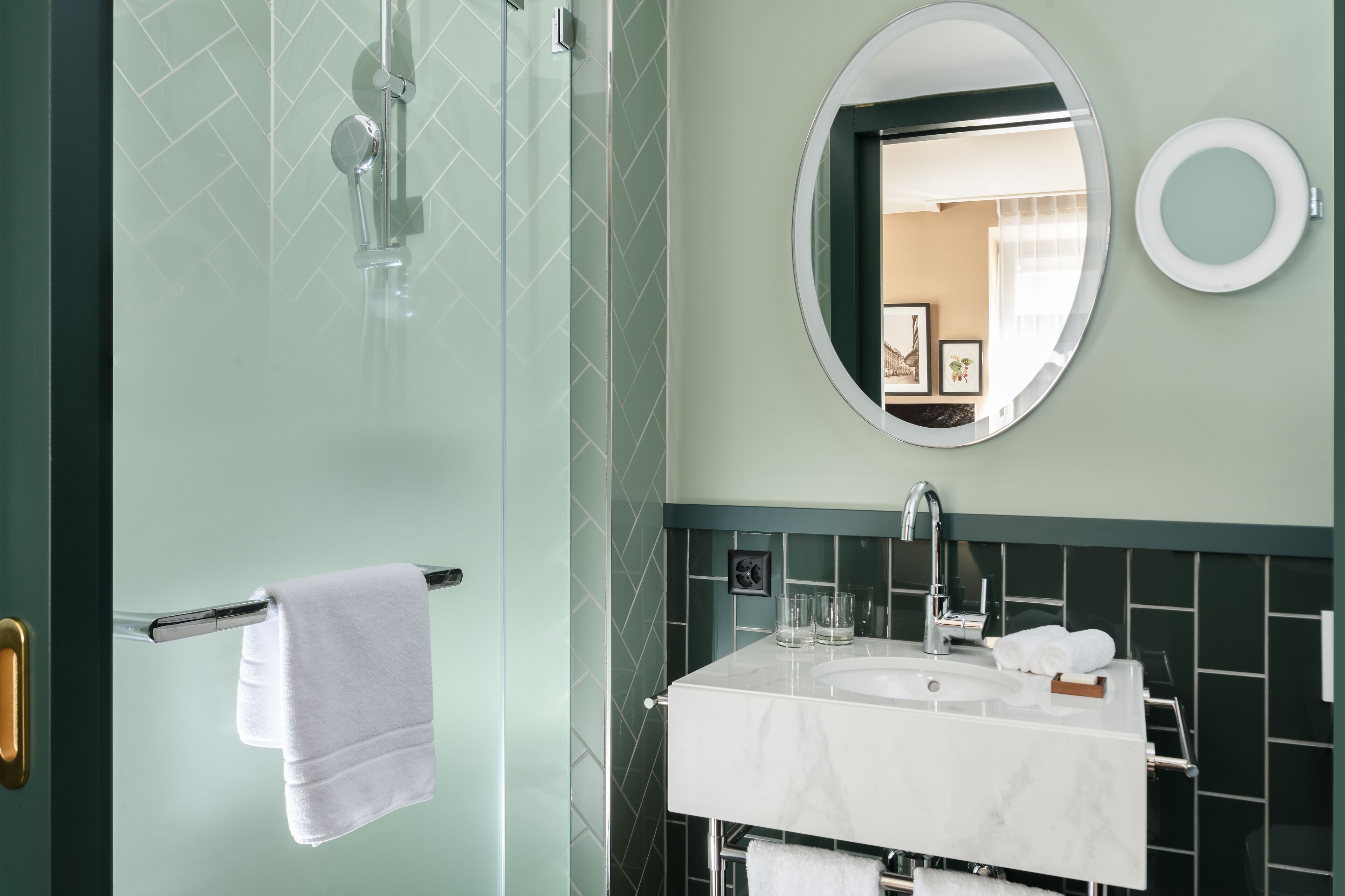A bathroom with a glass shower door, a white sink with a marble countertop, and a round mirror.
