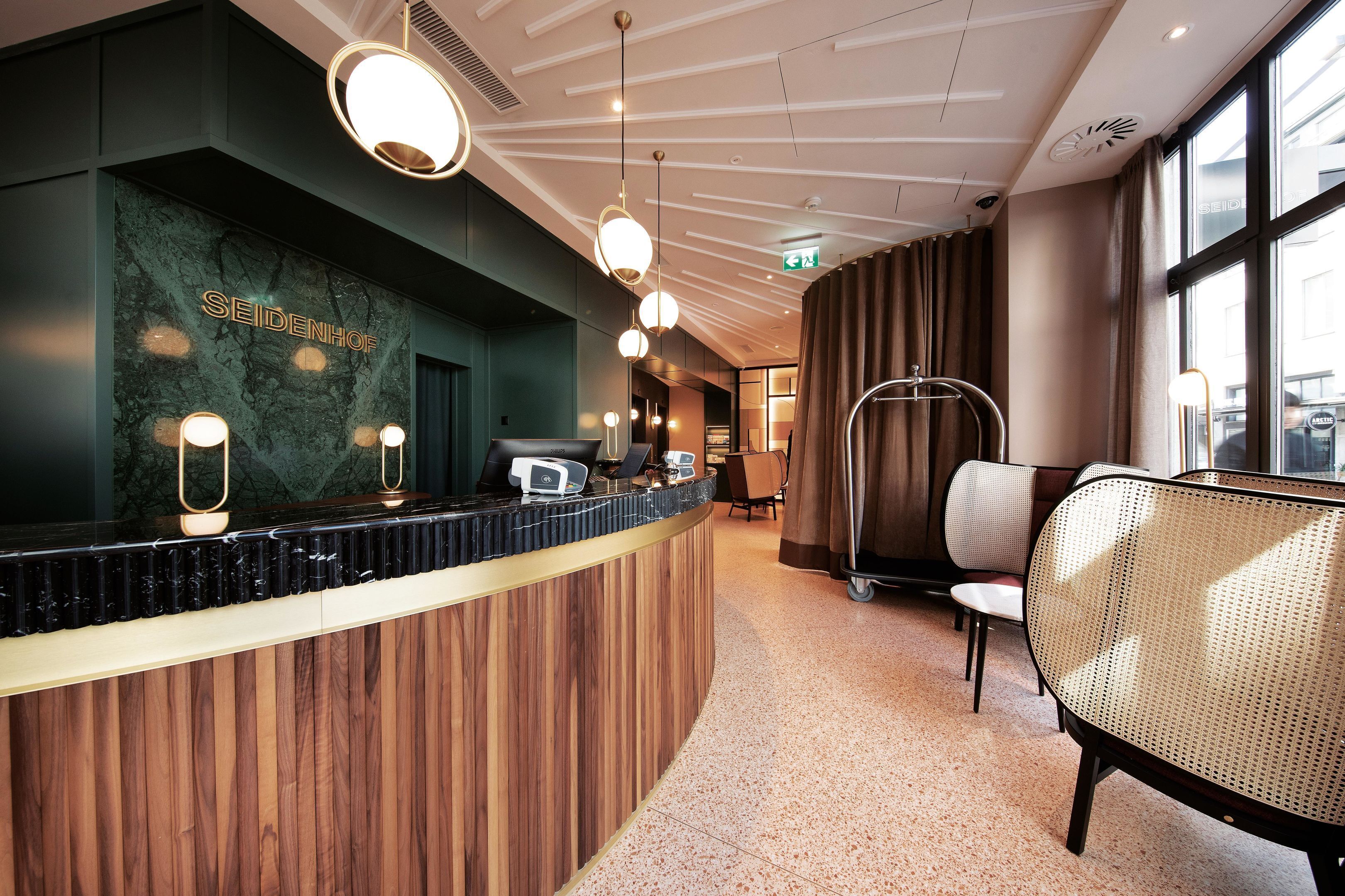 Un comptoir d’accueil avec un mur en marbre, des panneaux en bois et des luminaires suspendus.