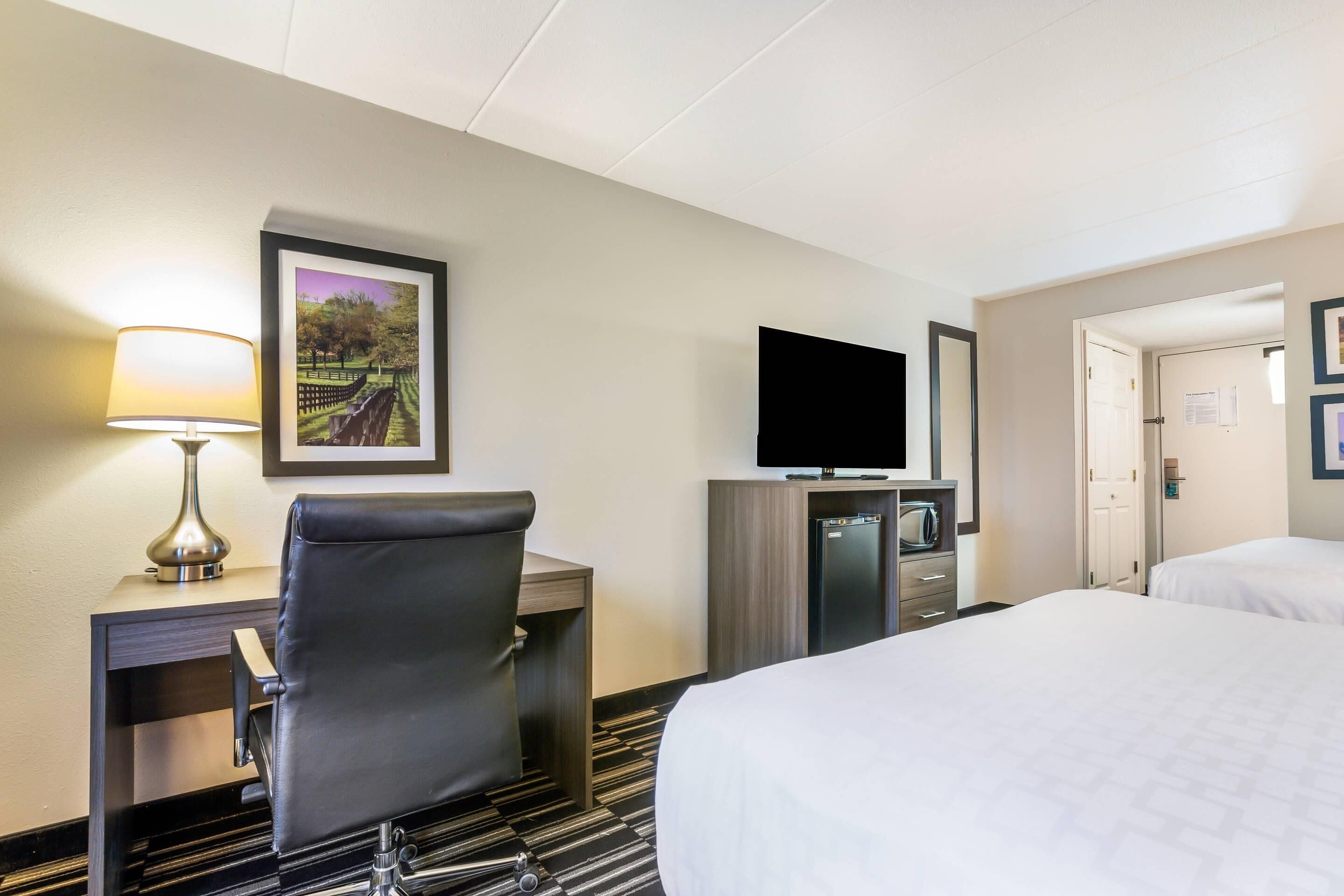 A hotel room with a desk, chair, TV, minibar, and two beds.