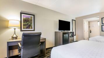 A hotel room with a desk, chair, TV, minibar, and two beds.