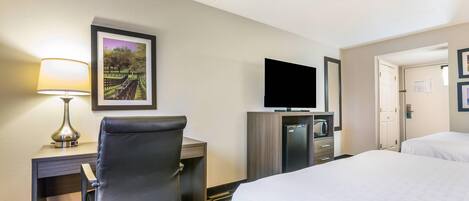 A hotel room with a desk, chair, TV, minibar, and two beds.
