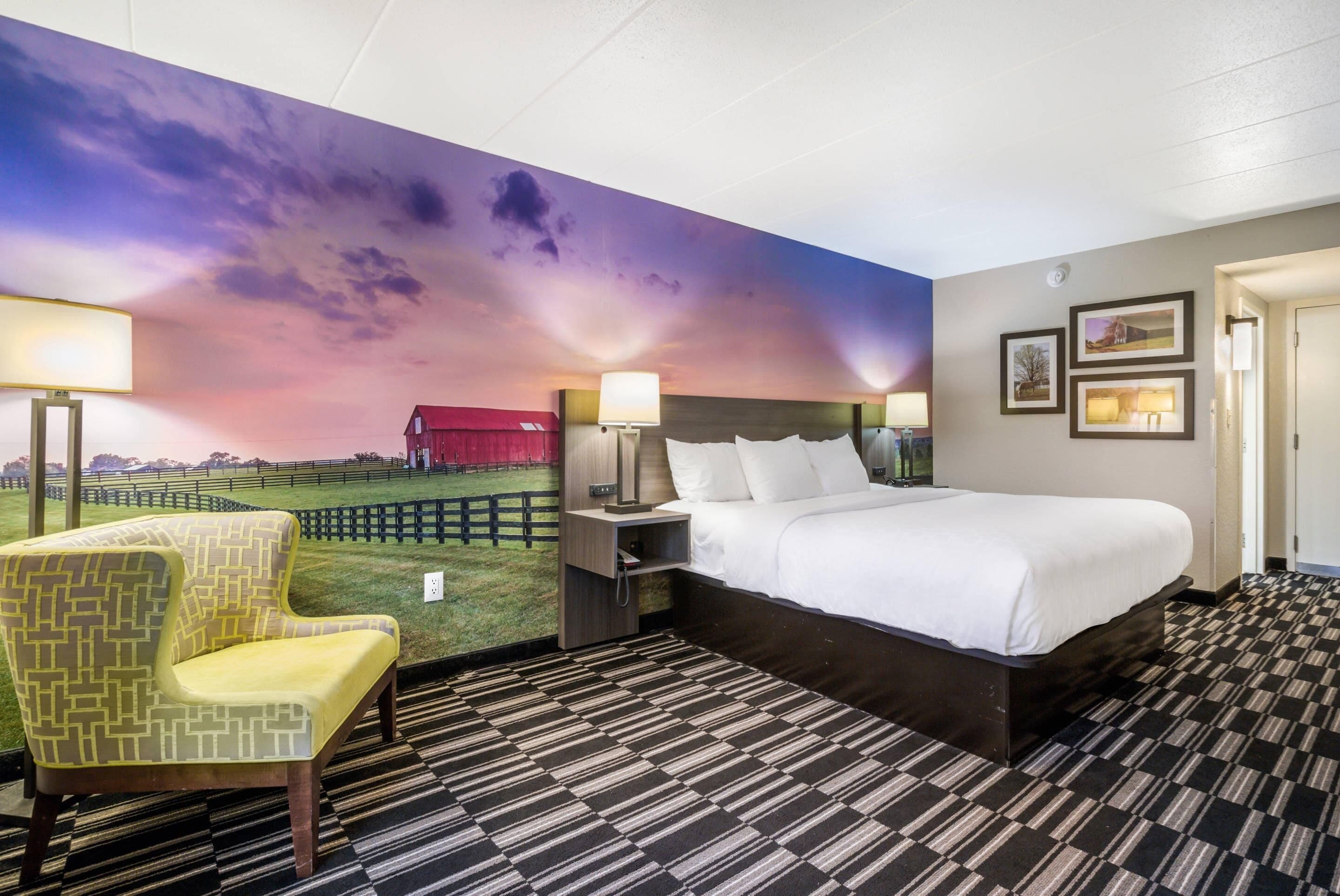 Ein Hotelzimmer mit einem großen Bett, einem Sessel, einem Nachttisch und einem Wandbild.