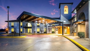Un hotel con acceso cubierto, una torre de campanas y aparcamiento.