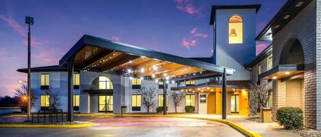 A hotel with a covered entrance, a bell tower, and a parking lot.