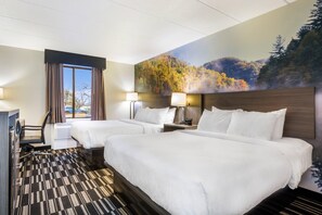 A hotel room with two beds, a desk, a chair, a TV, and a large painting of a forest.