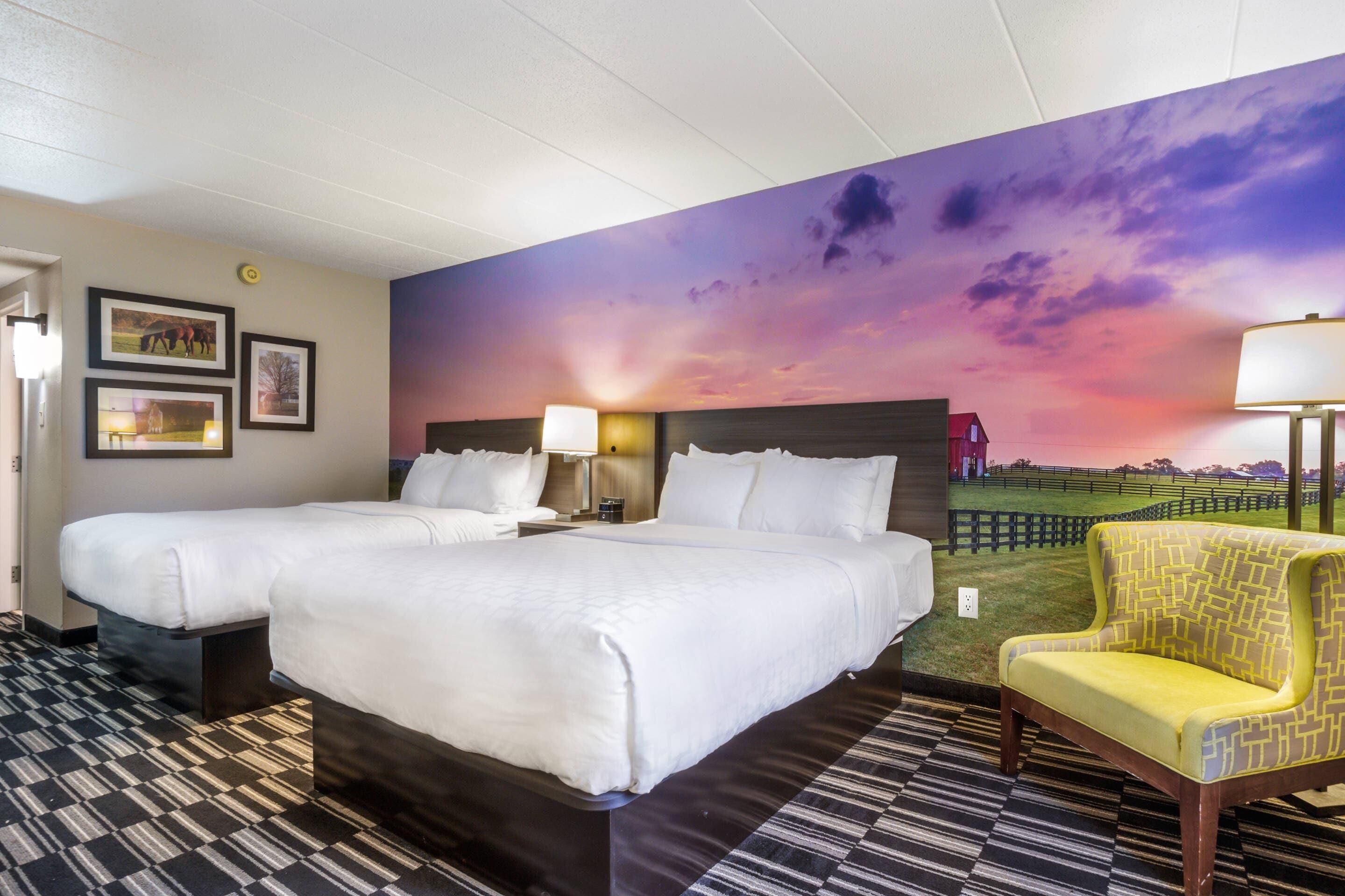 A hotel room with two beds, a large mural of a sunset, a patterned floor, and a yellow armchair.