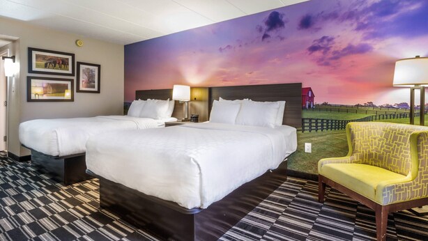 Quarto de hotel com duas camas, um grande mural do pôr do sol, um piso estampado e uma poltrona amarela.