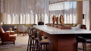 A modern bar area with a marble countertop, wooden stools, and a decorative wooden sculpture.