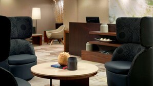 A modern hotel lobby with a round table, two armchairs, a reception desk, and a lamp.