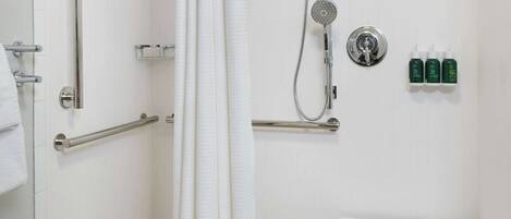 A modern bathroom with a walk-in shower, grab bars, a white sink, and a small table.