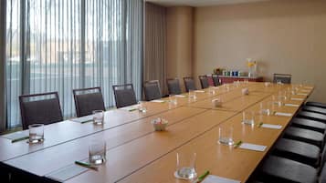 A conference room with a long table, chairs, and a view of the outdoors through large windows.