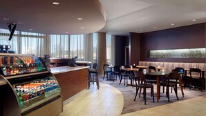 A modern hotel lobby with a curved reception desk, a beverage dispenser, and a seating area with tables and chairs.
