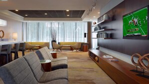 A modern hotel lobby with a long reception desk, comfortable seating, a large flat-screen TV, and a large window with sheer curtains.