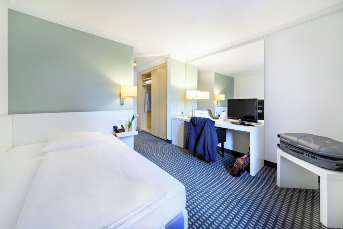 Ein Hotelzimmer mit Bett, Schreibtisch, Fernseher und Spiegel.